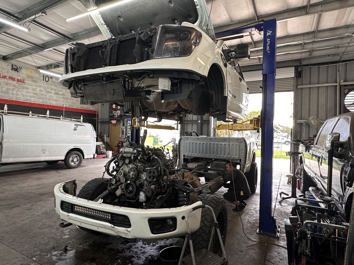 A white pickup truck raised on a lift with its front end and engine bay opened up
