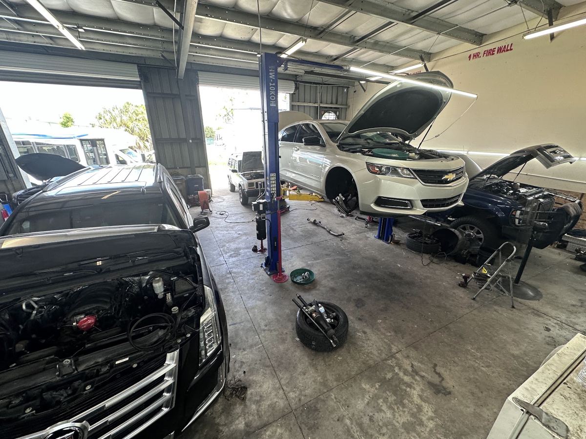 Shop bay with a black SUV with the hood open and a white sedan on a lift