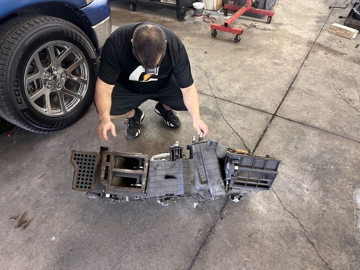 A shop worker reassembling dashboard and console parts on the floor next to a truck wheel
